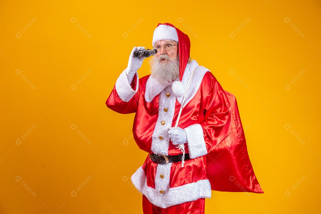 Foto de estúdio do Papai Noel olhando através de binóculos isolados em fundo amarelo