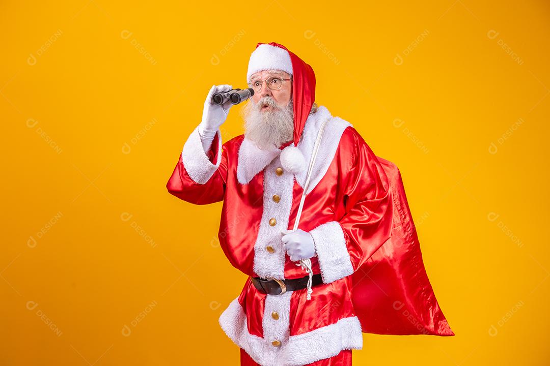 Foto de estúdio do Papai Noel olhando através de binóculos isolados em fundo amarelo
