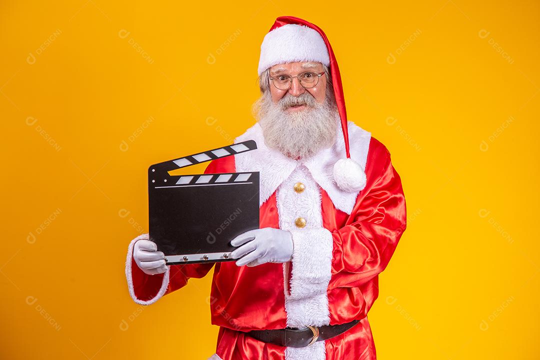 É hora de alguma ação. Alegre idoso Papai Noel posando com uma claquete.