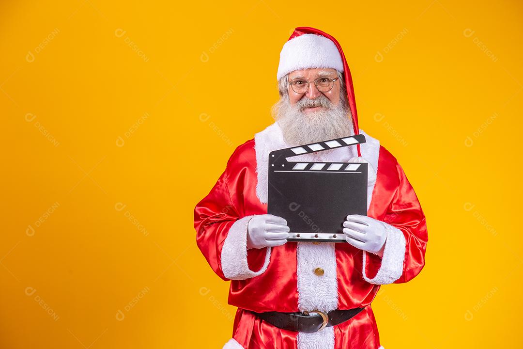 É hora de alguma ação. Alegre idoso Papai Noel posando com uma claquete.