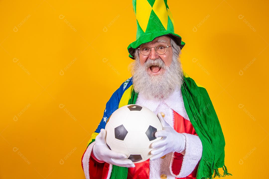 Papai Noel é fã do Brasil. Papai Noel torcedor da seleção brasileira. Campeonato esportivo. Papai Noel com a bandeira brasileira e uma bola. Partida de futebol.