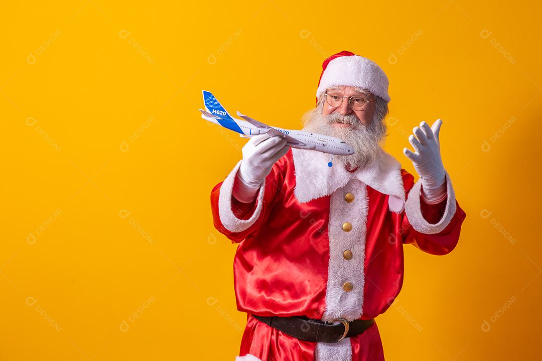 Papai Noel segurando um aviãozinho de brinquedo em fundo amarelo. conceito de viagem de natal