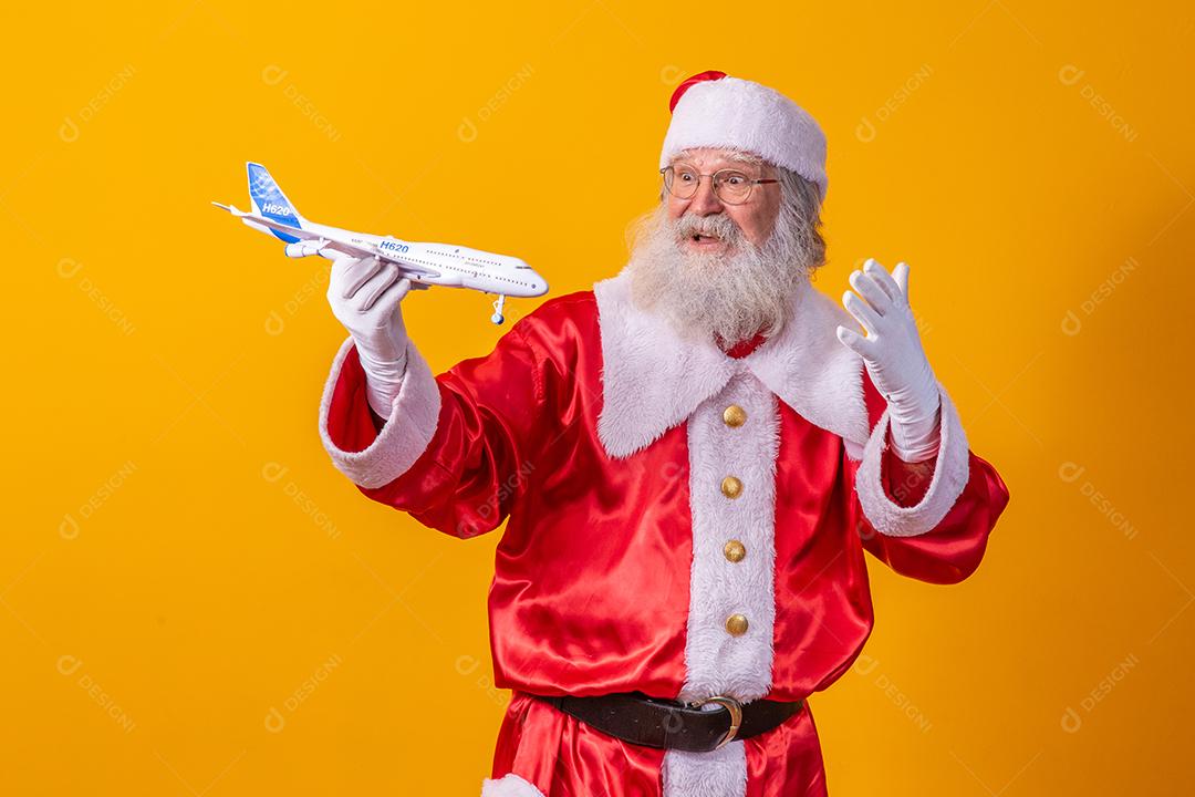 Papai Noel segurando um aviãozinho de brinquedo em fundo amarelo. conceito de viagem de natal