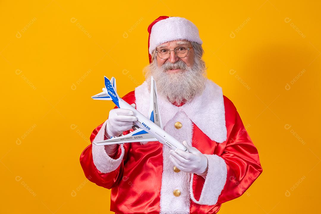 Papai Noel segurando um aviãozinho de brinquedo em fundo amarelo. conceito de viagem de natal