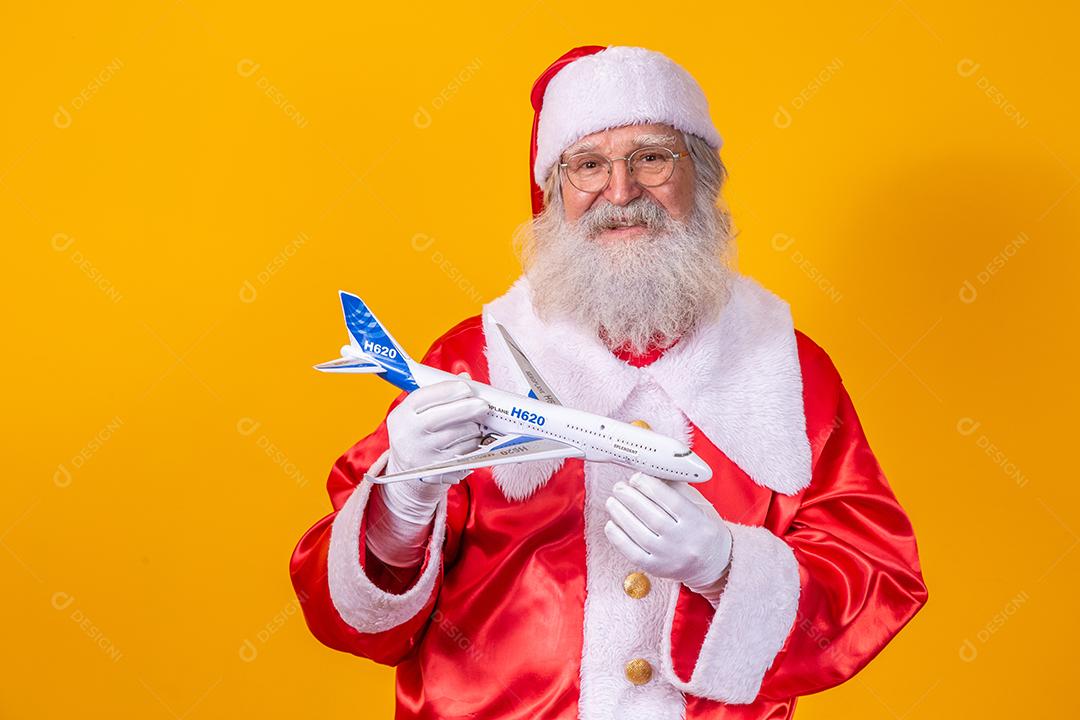 Papai Noel segurando um aviãozinho de brinquedo em fundo amarelo. conceito de viagem de natal