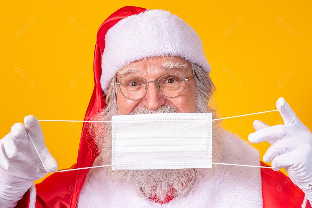 O verdadeiro Papai Noel com fundo amarelo, segurando uma máscara protetora, óculos e chapéu. Natal com distanciamento social. Covid-19