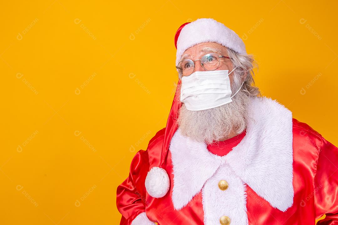 Verdadeiro Papai Noel com fundo amarelo, usando uma máscara protetora, óculos e chapéu. Natal com distanciamento social. Covid-19