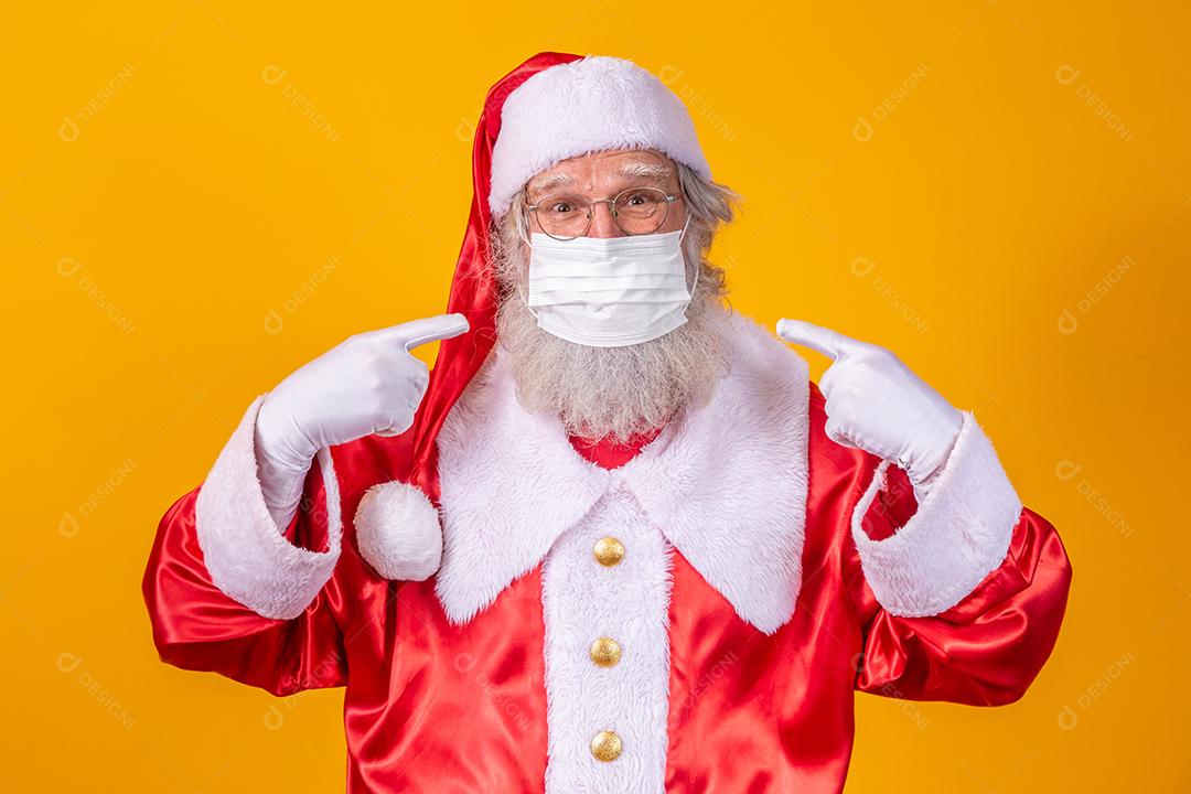 Verdadeiro Papai Noel com fundo amarelo, usando uma máscara protetora, óculos e chapéu. Natal com distanciamento social. Covid-19