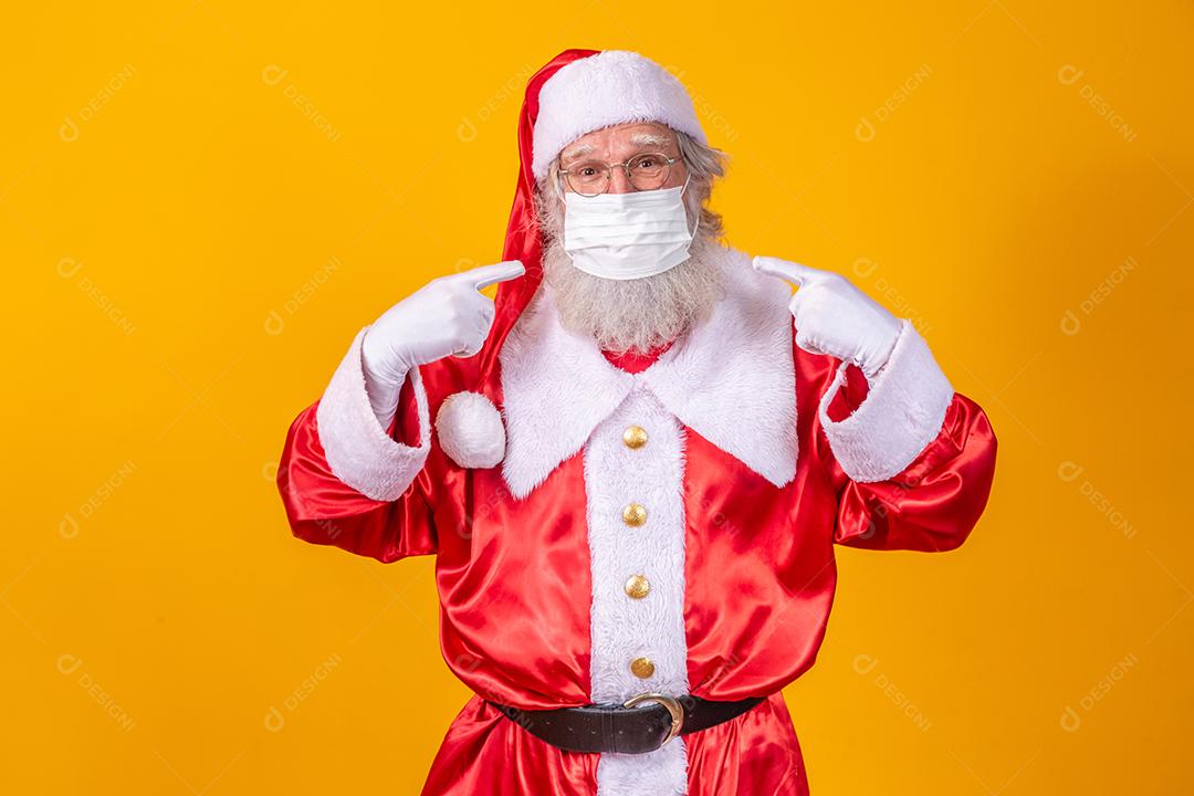 Verdadeiro Papai Noel com fundo amarelo, usando uma máscara protetora, óculos e chapéu. Natal com distanciamento social. Covid-19