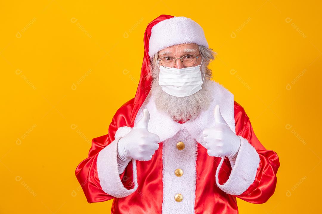 Verdadeiro Papai Noel com fundo amarelo, usando uma máscara protetora, óculos e chapéu. Natal com distanciamento social. Covid-19