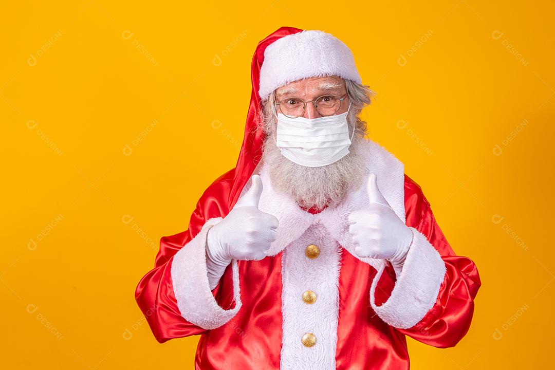 Verdadeiro Papai Noel com fundo amarelo, usando uma máscara protetora, óculos e chapéu. Natal com distanciamento social. Covid-19