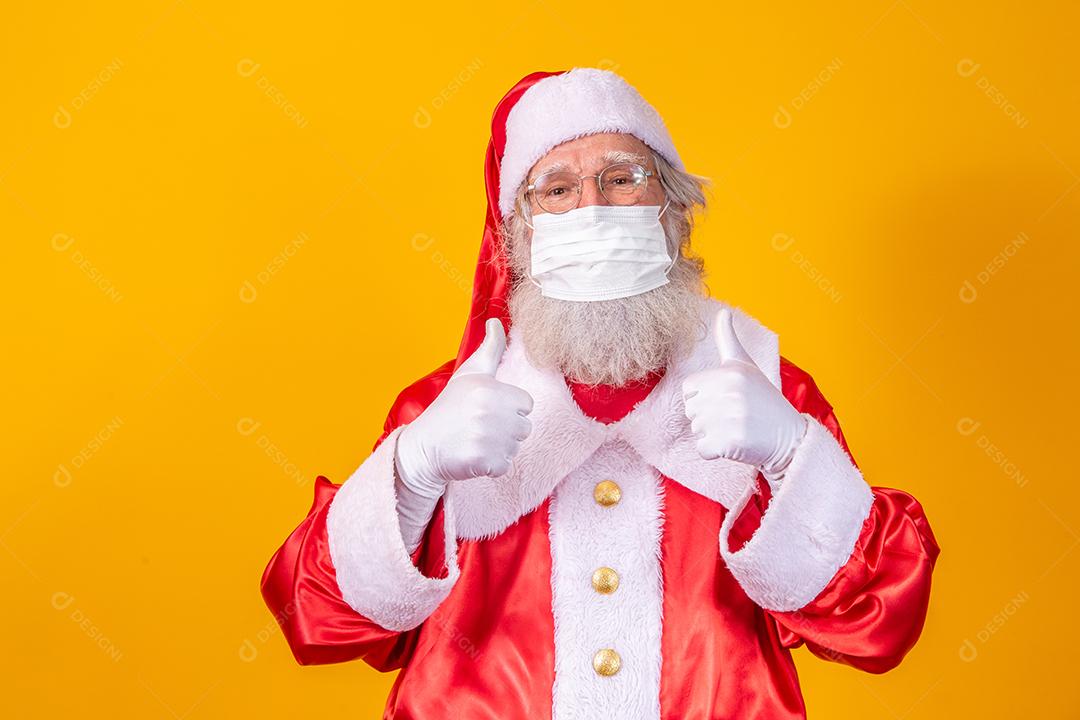 Verdadeiro Papai Noel com fundo amarelo, usando uma máscara protetora, óculos e chapéu. Natal com distanciamento social. Covid-19