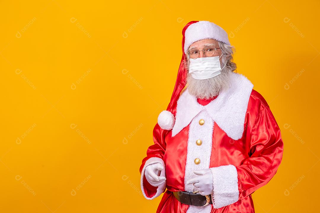 Verdadeiro Papai Noel com fundo amarelo, usando uma máscara protetora, óculos e chapéu. Natal com distanciamento social. Covid-19