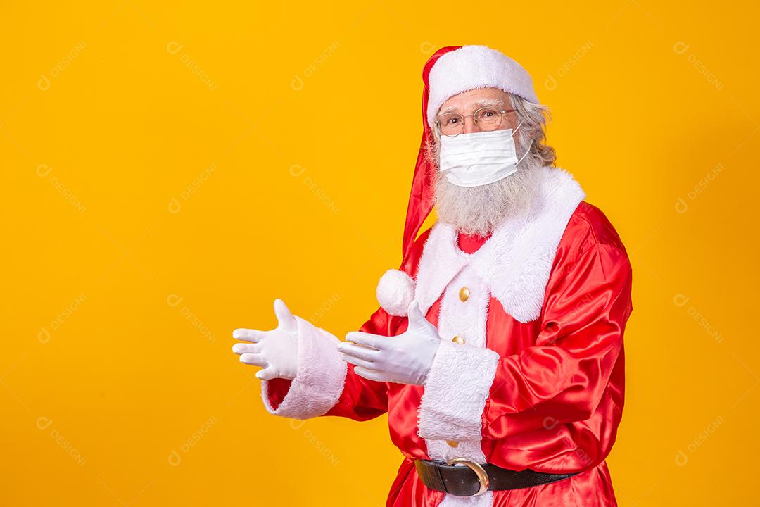 Verdadeiro Papai Noel com fundo amarelo, usando uma máscara protetora, óculos e chapéu. Natal com distanciamento social. Covid-19