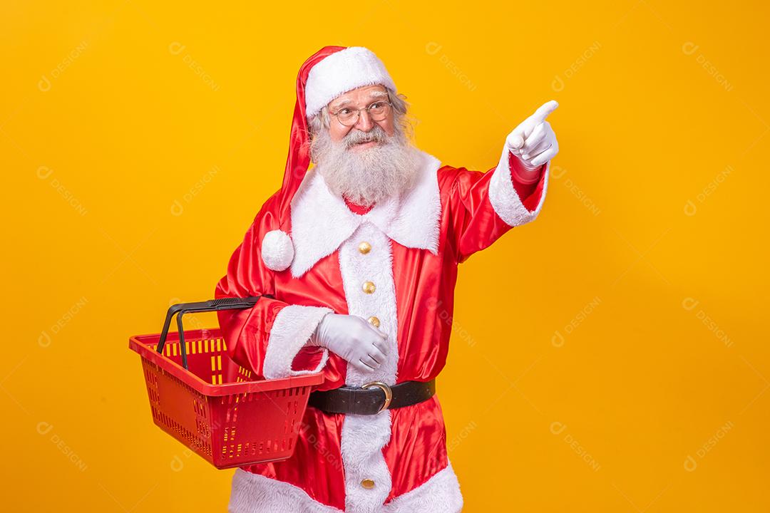 Papai Noel segurando uma cesta de compras vazia, olhando para a câmera sorrindo.