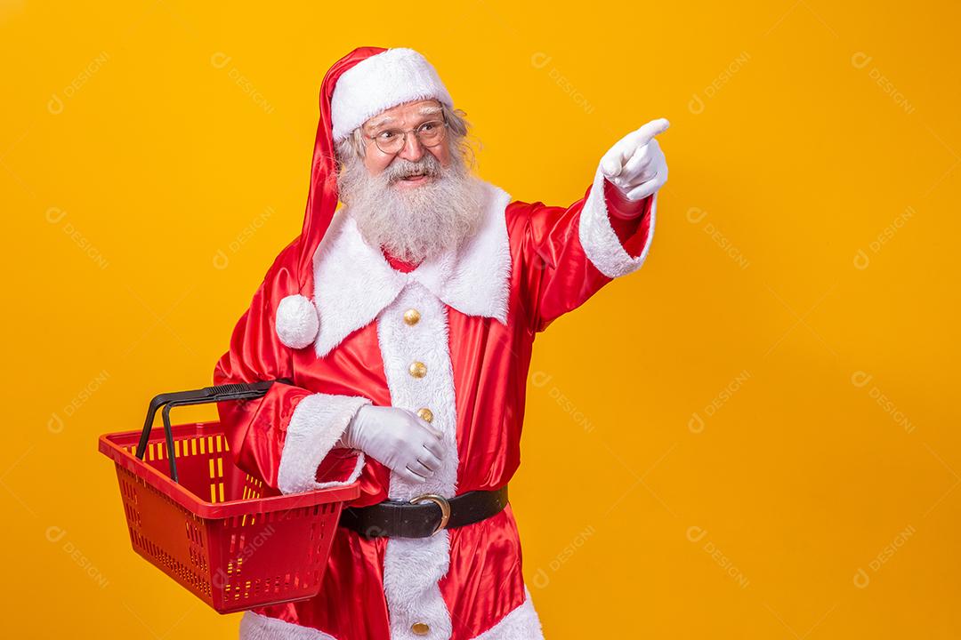 Papai Noel segurando uma cesta de compras vazia, olhando para a câmera sorrindo.