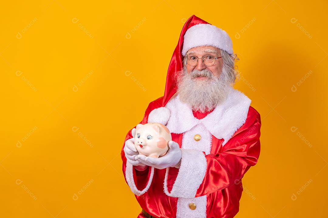 Papai Noel colocando moedas em um cofrinho de cerâmica. Conceito de poupança para o final do ano. Gastando no Natal. Gasto em presentes de Natal.