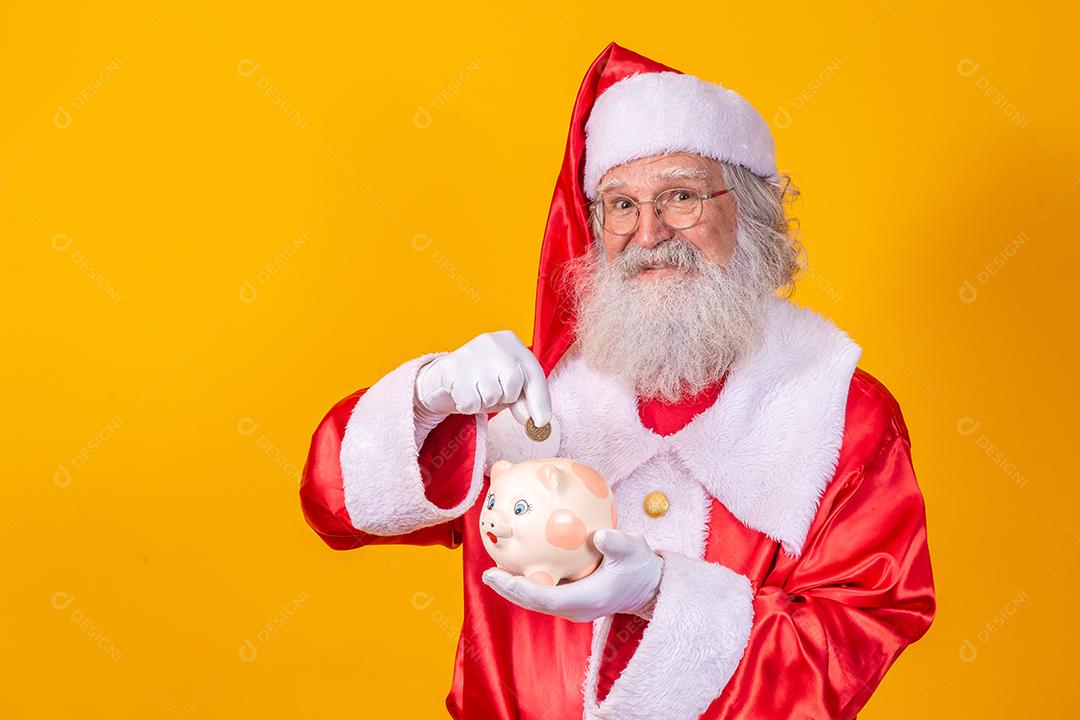 Papai Noel colocando moedas em um cofrinho de cerâmica. Conceito de poupança para o final do ano. Gastando no Natal. Gasto em presentes de Natal.