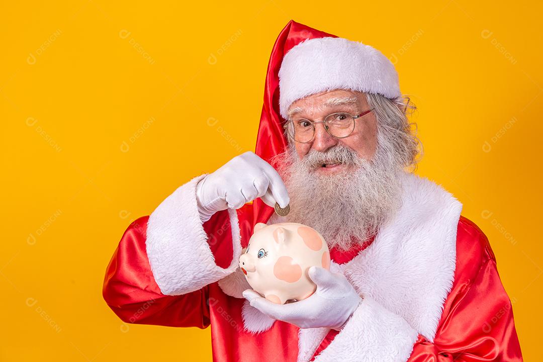 Papai Noel colocando moedas em um cofrinho de cerâmica. Conceito de poupança para o final do ano. Gastando no Natal. Gasto em presentes de Natal.