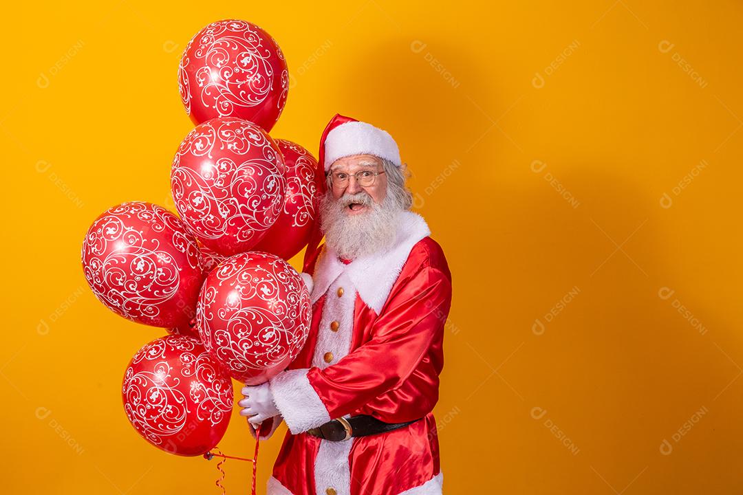 Papai Noel em fundo amarelo segurando balões vermelhos.
