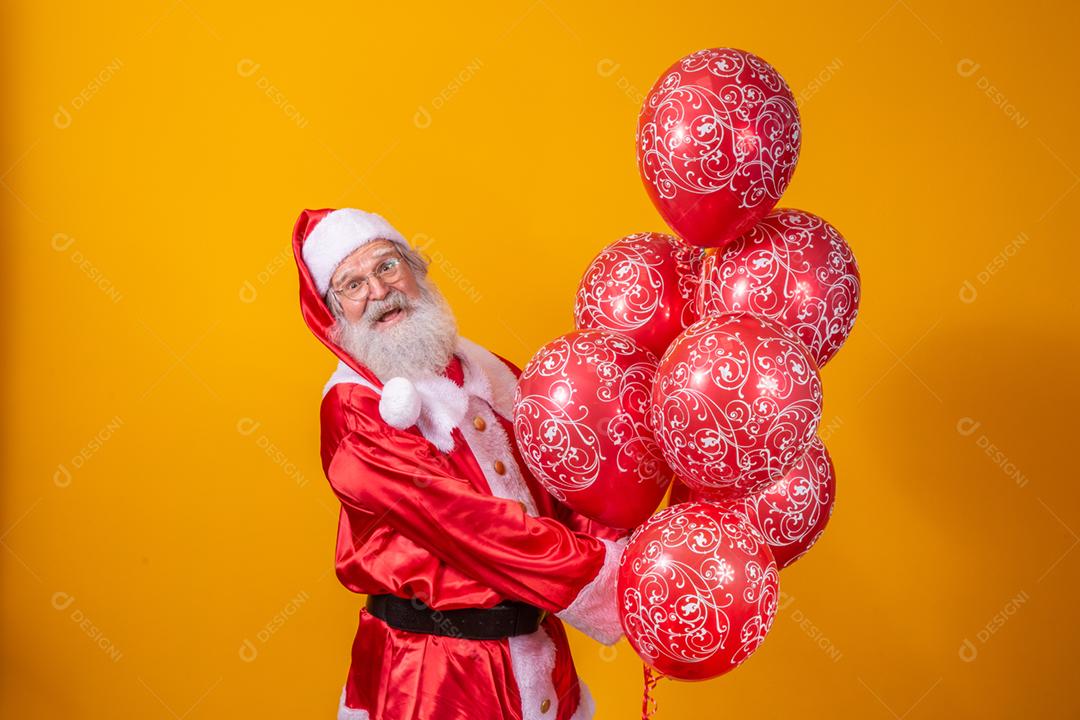 Papai Noel em fundo amarelo segurando balões vermelhos.