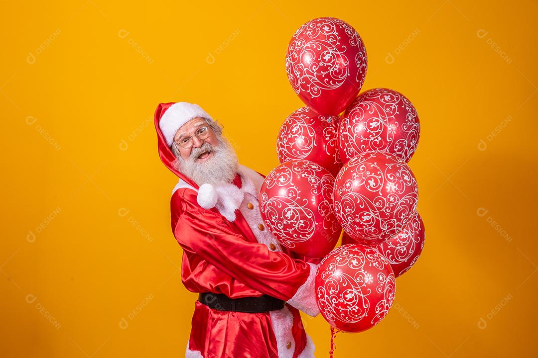 Papai Noel em fundo amarelo segurando balões vermelhos.