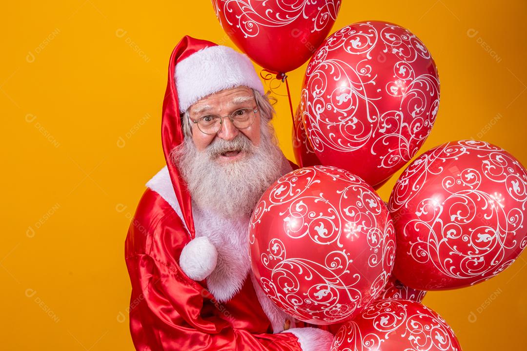 Papai Noel em fundo amarelo segurando balões vermelhos.