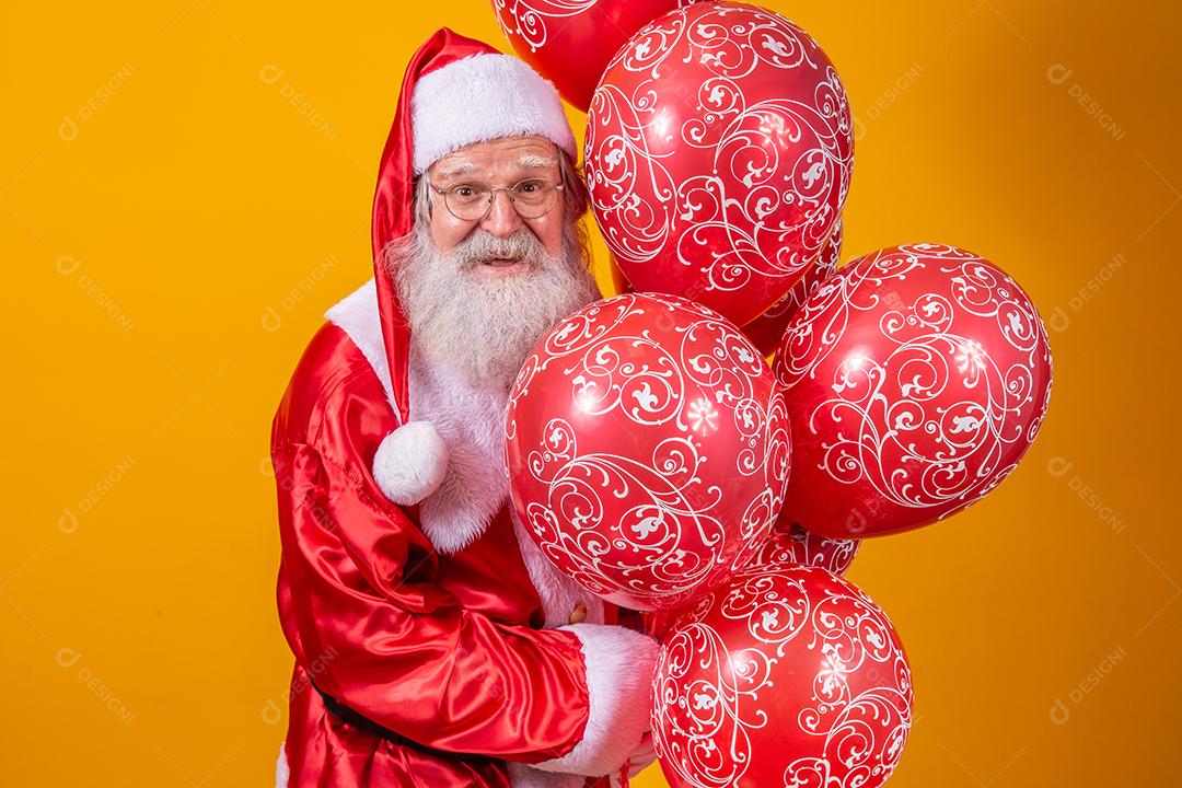 Papai Noel em fundo amarelo segurando balões vermelhos.