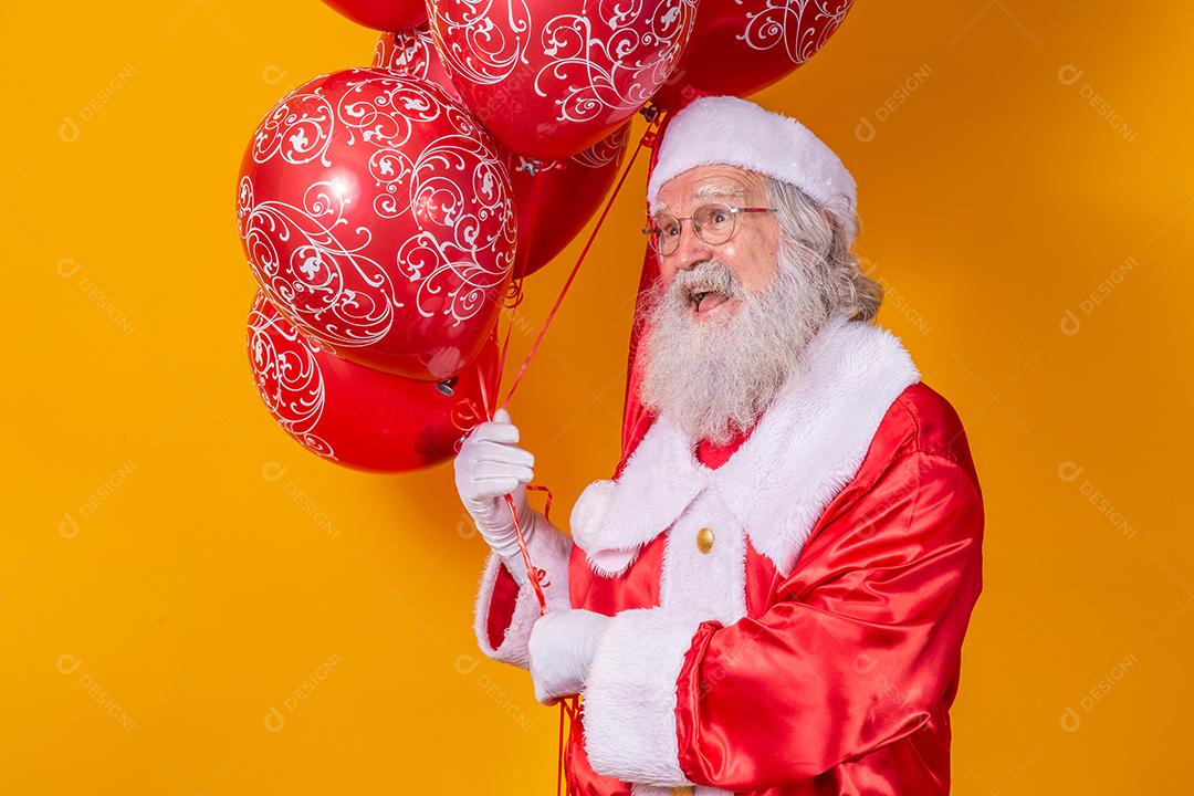 Papai Noel em fundo amarelo segurando balões vermelhos.