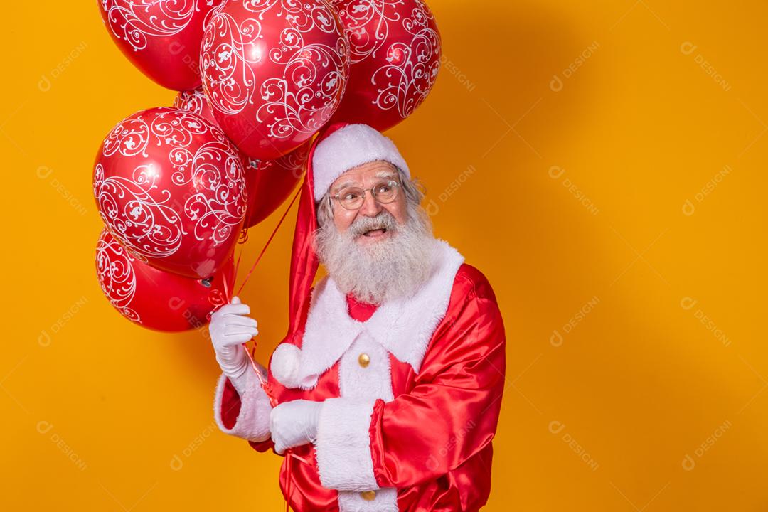 Papai Noel em fundo amarelo segurando balões vermelhos.
