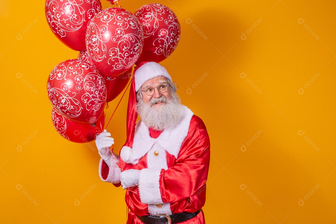 Papai Noel em fundo amarelo segurando balões vermelhos.