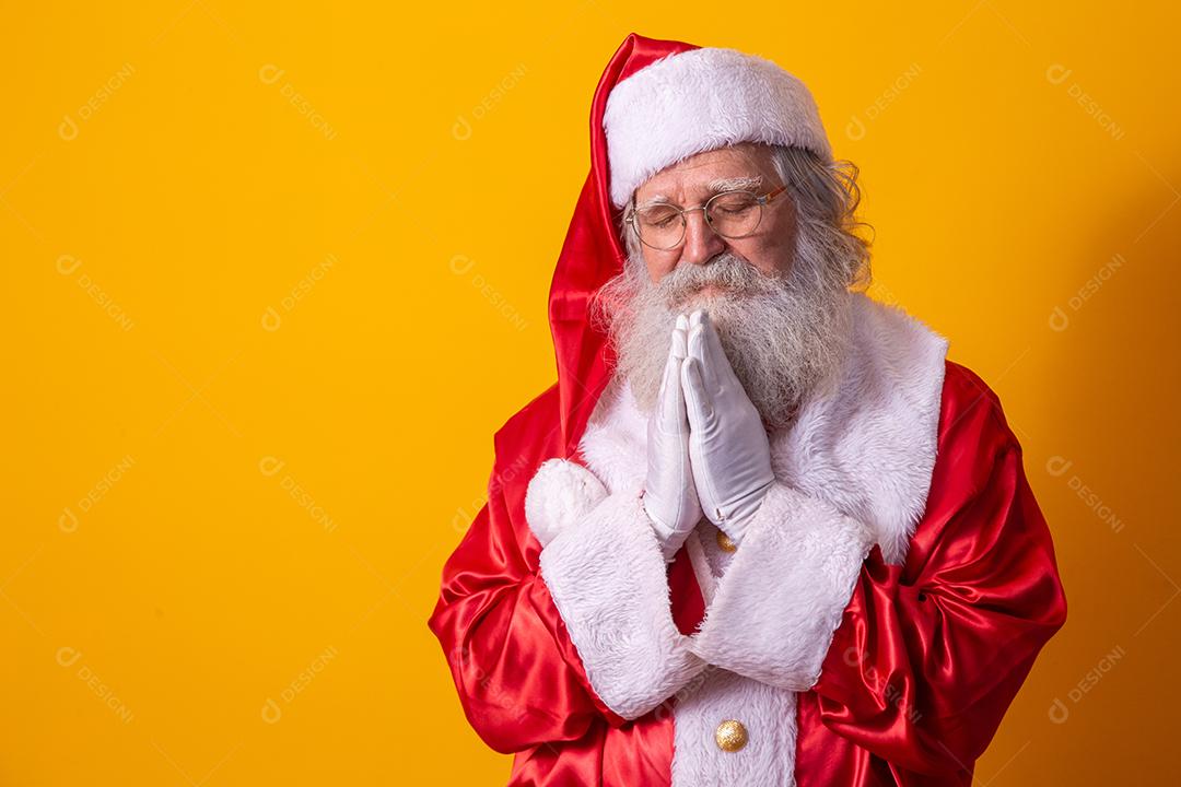Papai Noel rezando em fundo amarelo. Fé
