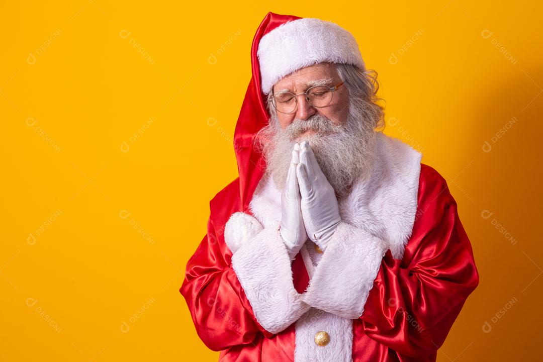 Papai Noel rezando em fundo amarelo. Fé