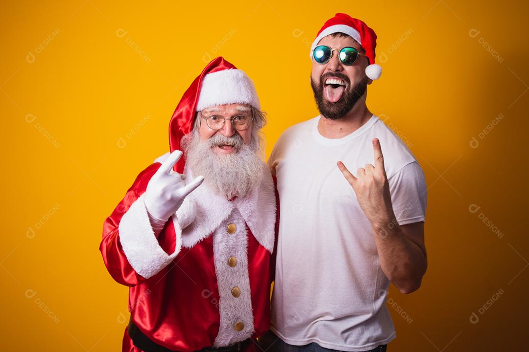 menino ao lado de Papai Noel fazendo sinal de rock in roll. Papai Noel é uma roca