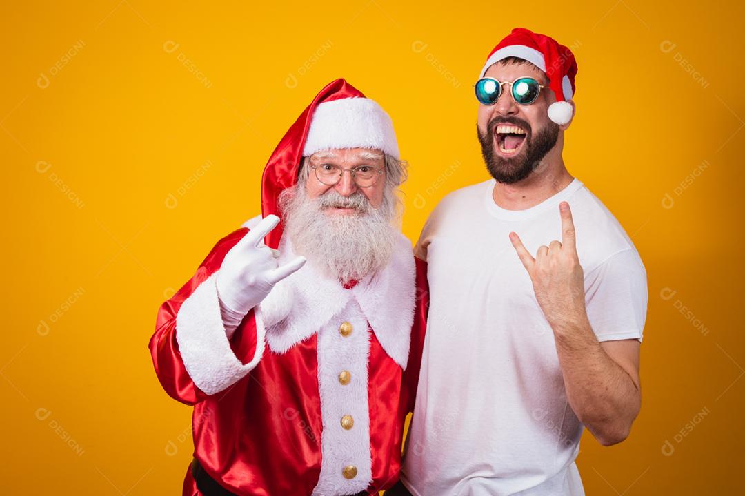 menino ao lado de Papai Noel fazendo sinal de rock in roll. Papai Noel é uma roca