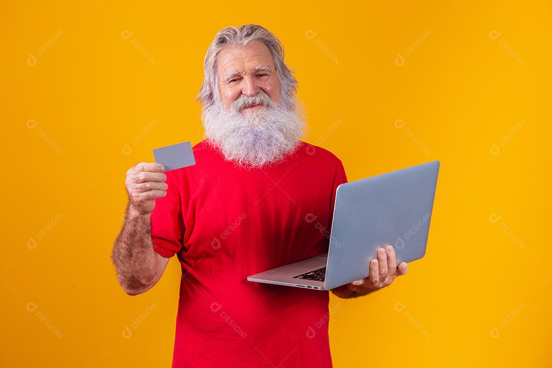 Homem em fundo amarelo mostrando cartão e fazendo uma chamada de vídeo no laptop