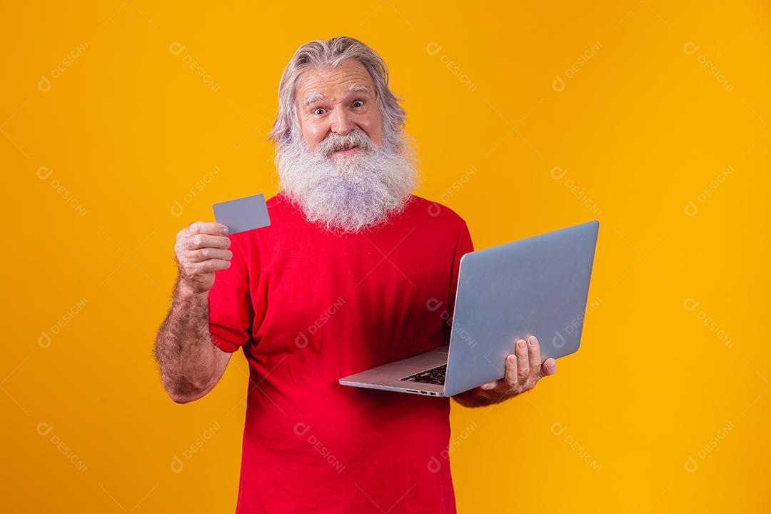 Homem em fundo amarelo mostrando cartão e fazendo uma chamada de vídeo no laptop