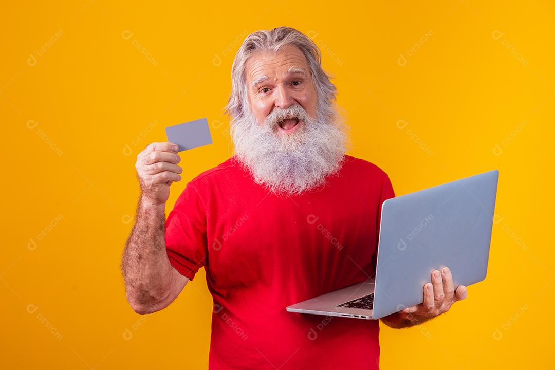 Homem em fundo amarelo mostrando cartão e fazendo uma chamada de vídeo no laptop