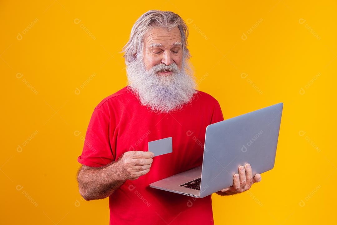Elderly man holding laptop computer and bank credit card. Online shopping transaction. Mobile banking cashless method.