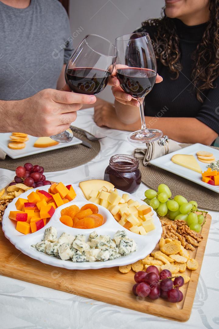 casal brindando com vinho e queijo no jantar. Aposte nos queijos