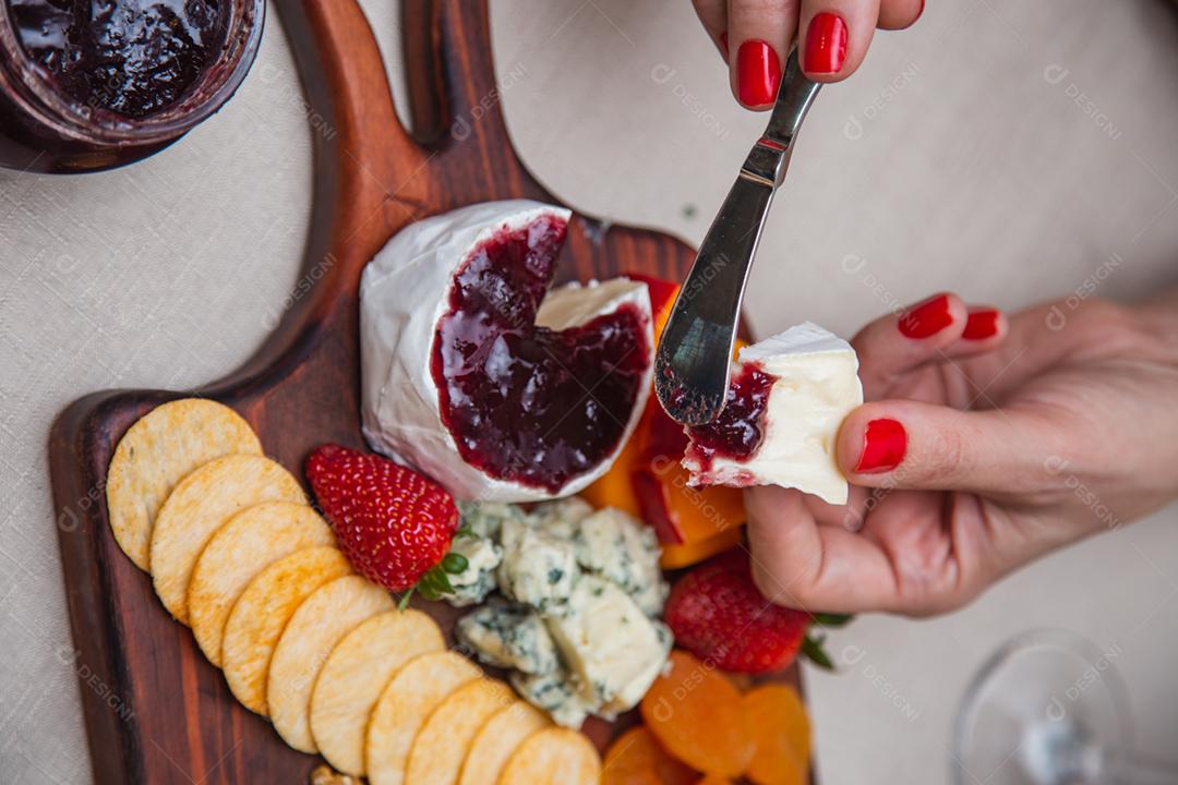 mãos passando geléia no queijo com vários queijos no fundo