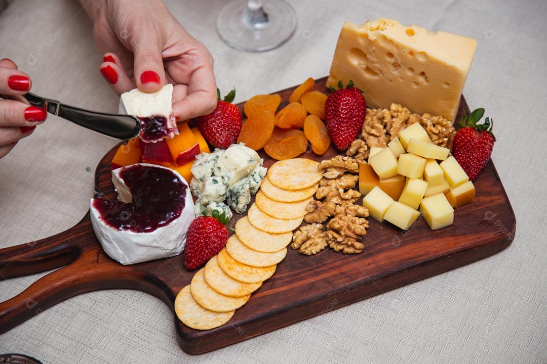 mãos passando geléia no queijo com vários queijos no fundo