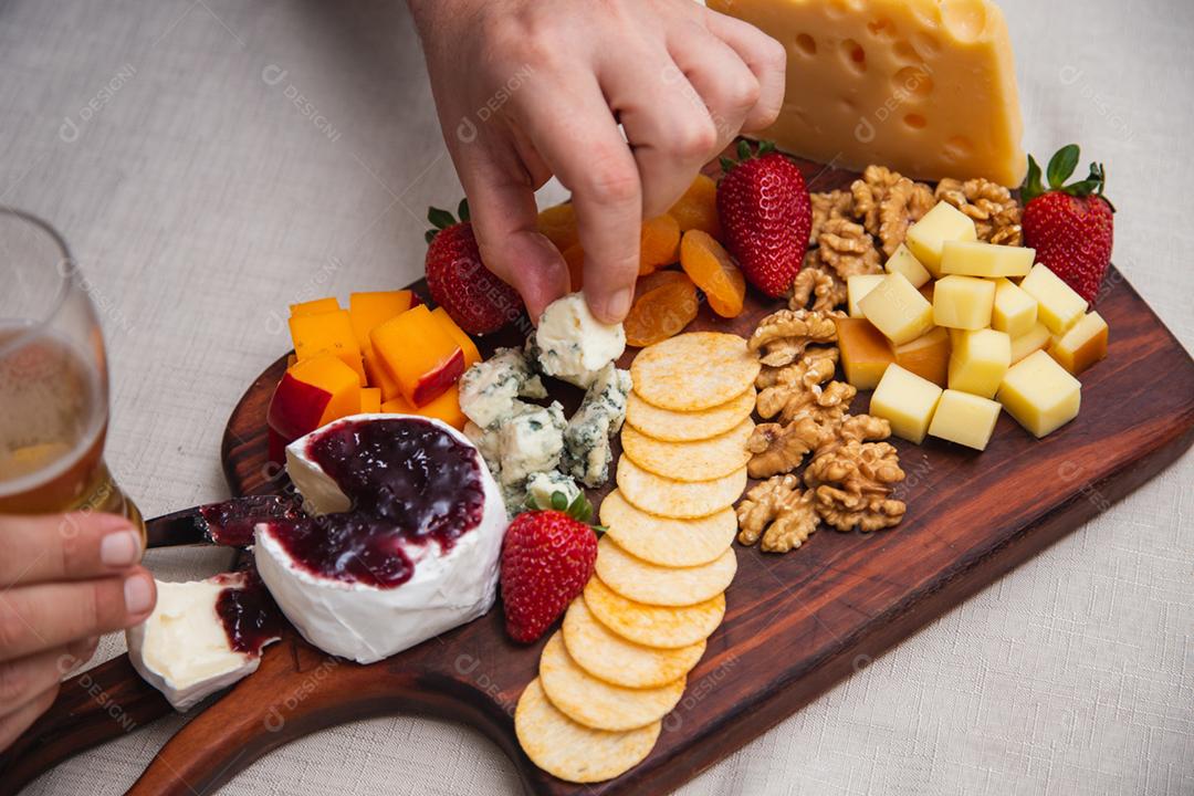 mãos passando geléia no queijo com vários queijos no fundo