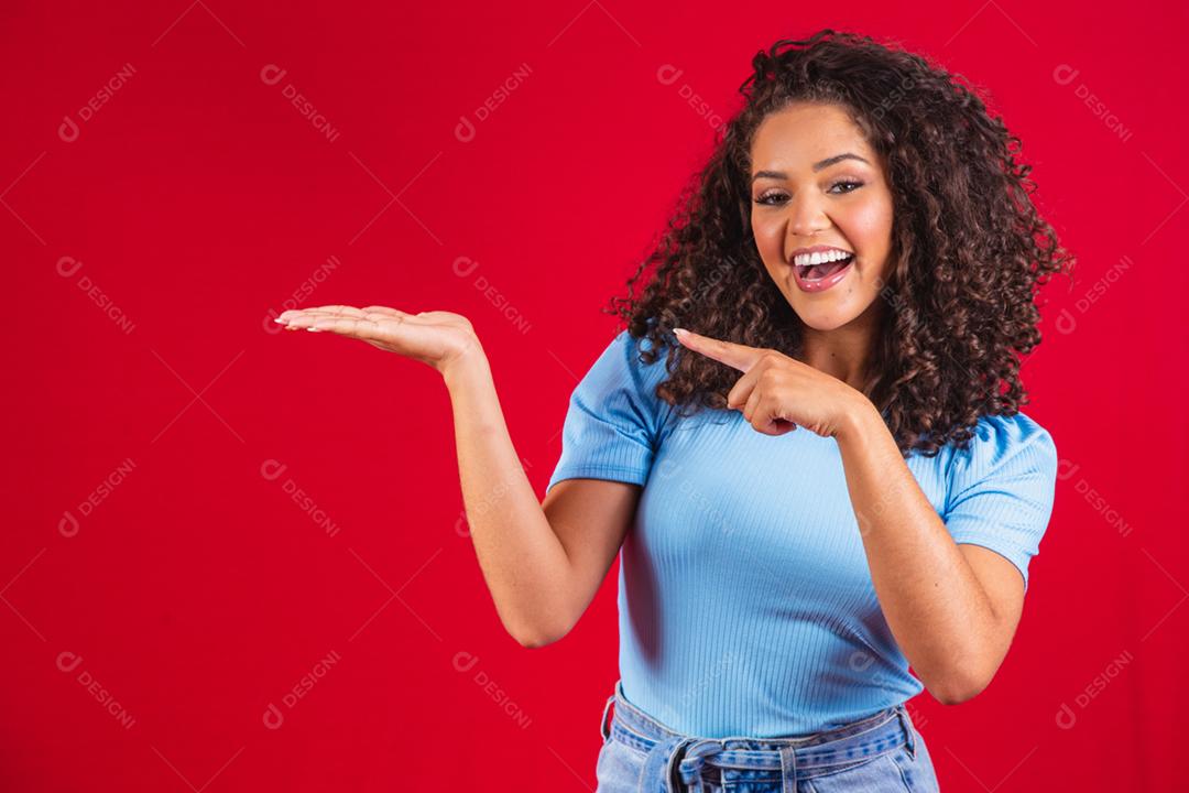 Alegre mulher afro aponta para o espaço da cópia, discute incrível