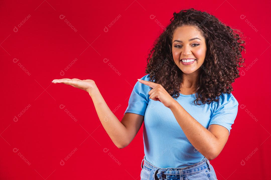 Alegre mulher afro aponta para o espaço da cópia, discute incrível