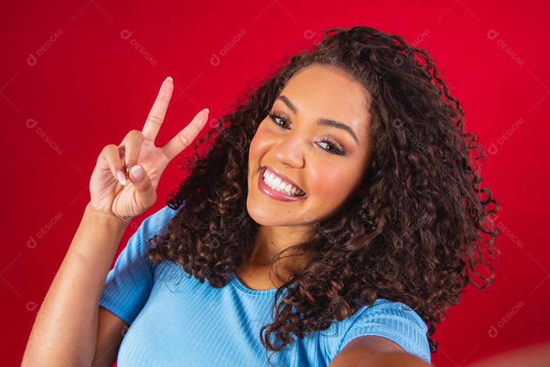 Retrato de jovem tomando selfie com sinal de mão de paz. afro