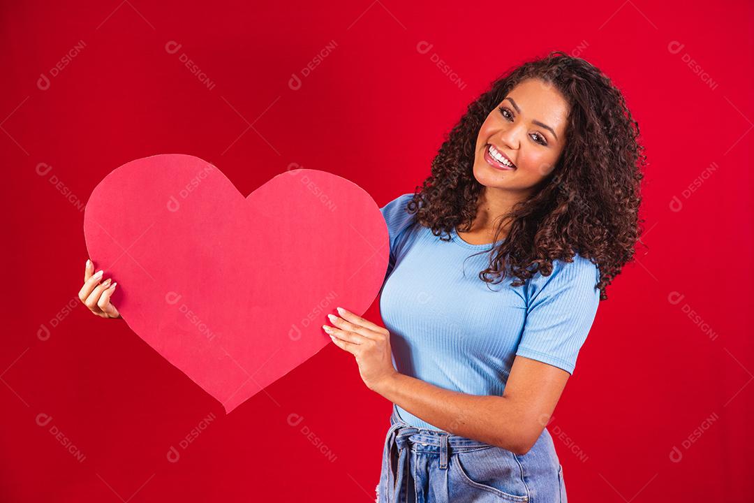 garota afro segurando nas mãos forma de coração amour isolado sobre fundo vermelho