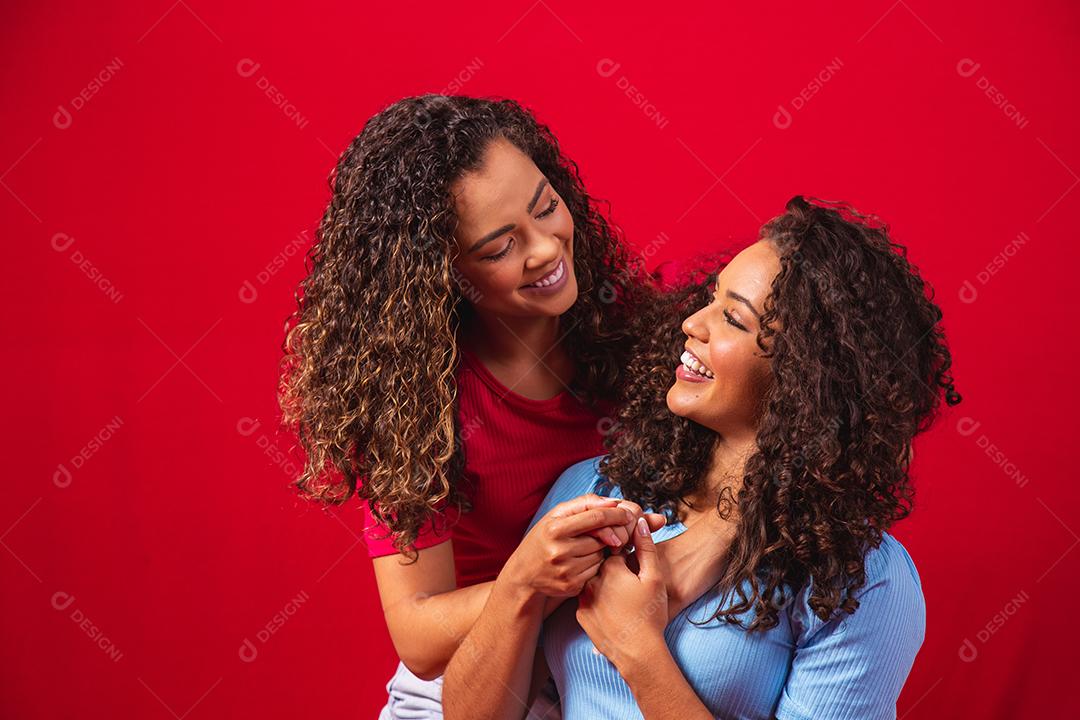 Retrato de casal de lésbicas jovens mulheres afro sobre fundo vermelho. conceito LGBT