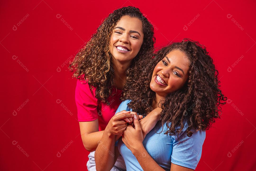 Retrato de casal de lésbicas jovens mulheres afro sobre fundo vermelho. conceito LGBT