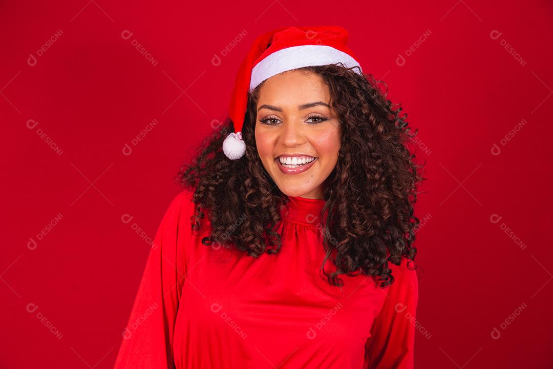 Feche a foto de uma jovem afro usando chapéu de Papai Noel isolado sobre fundo vermelho.